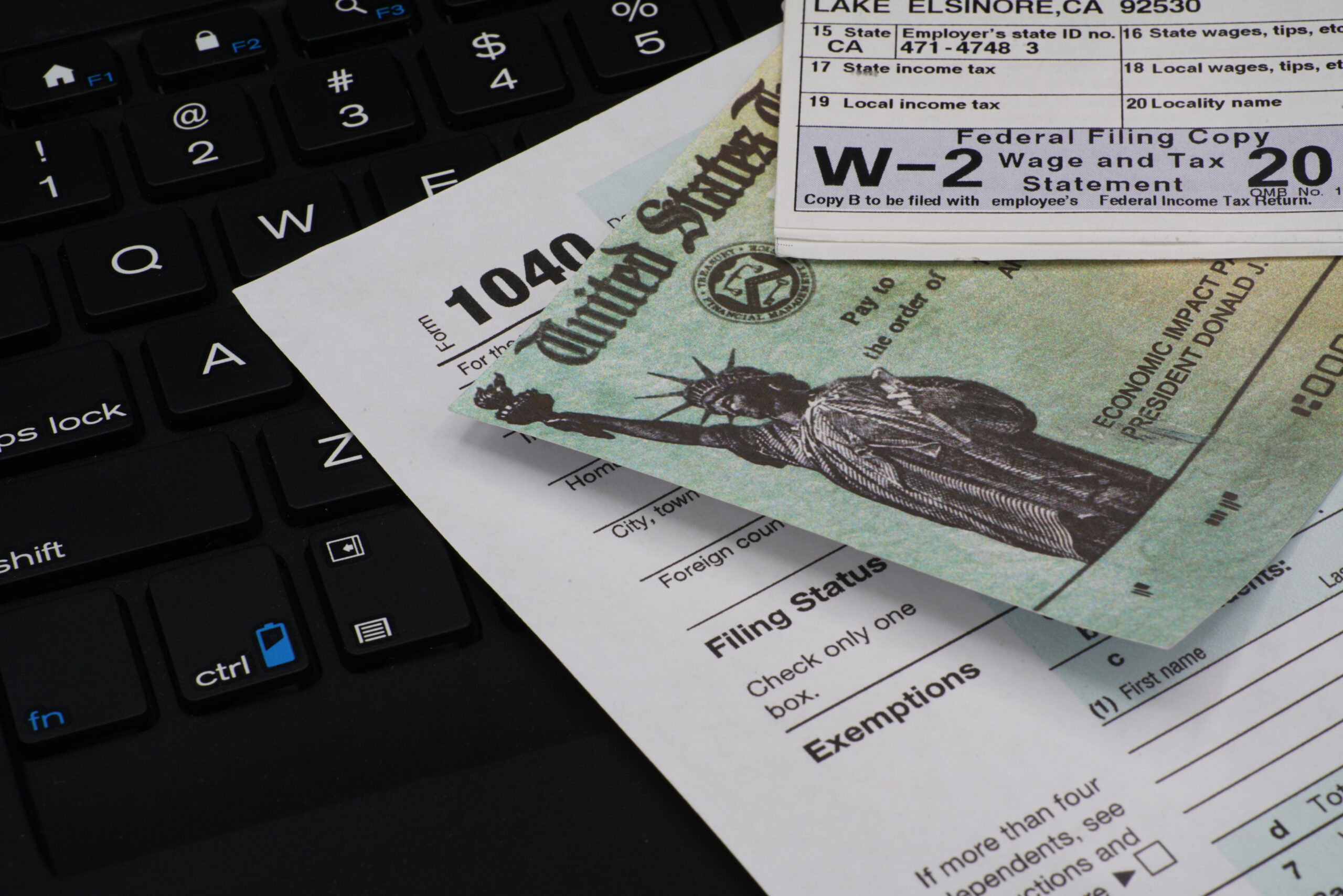 A 1040 form with a W-2 form and a United States check stacked on top, all of which are resting on a laptop keyboard.