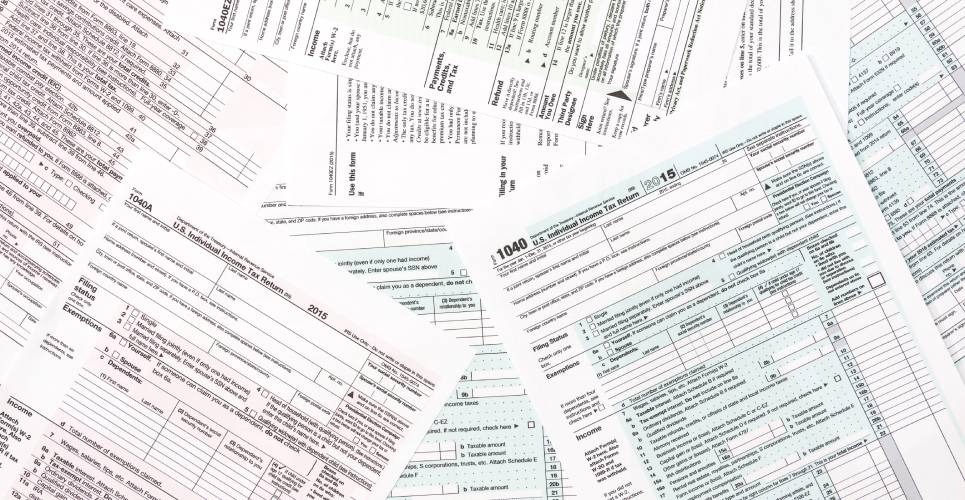 A stack of haphazardly laid out tax papers, including the 1040 tax return, as well as many other forms.