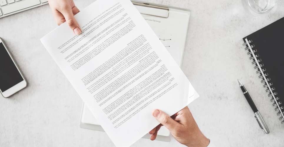 A close-up of two business people sitting on opposite sides of a marble desk, exchanging a small stack of documents.