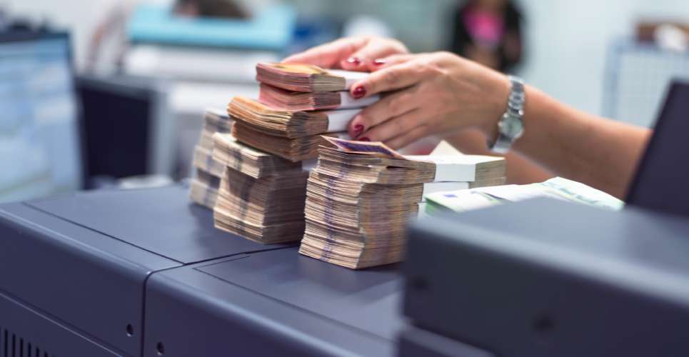 A bank employee wearing a watch setting out multiple stacks of bills bound with white bands on her desk.