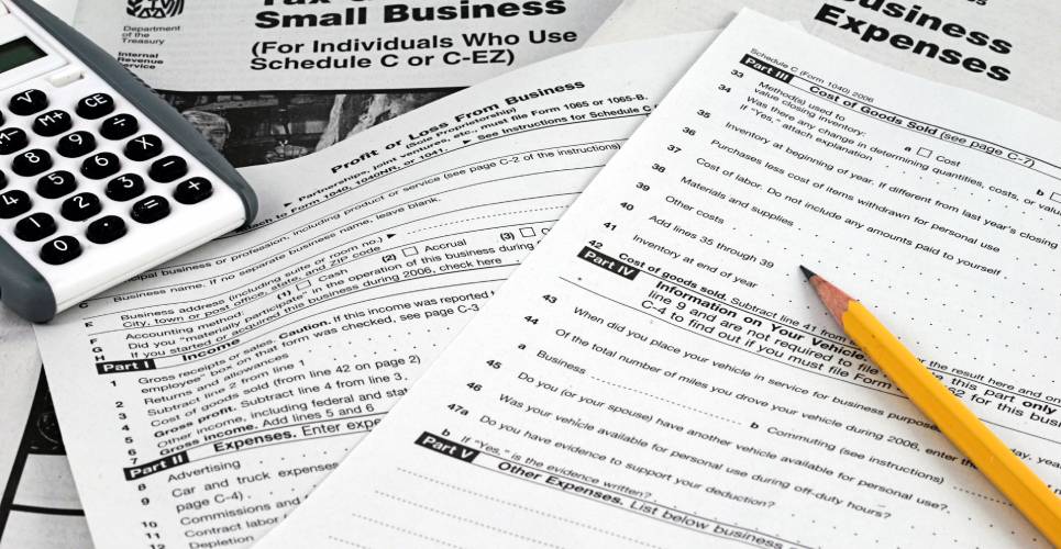 Multiple tax documents, including a tax guide for small businesses and a business expenses sheet, on a plain white table.