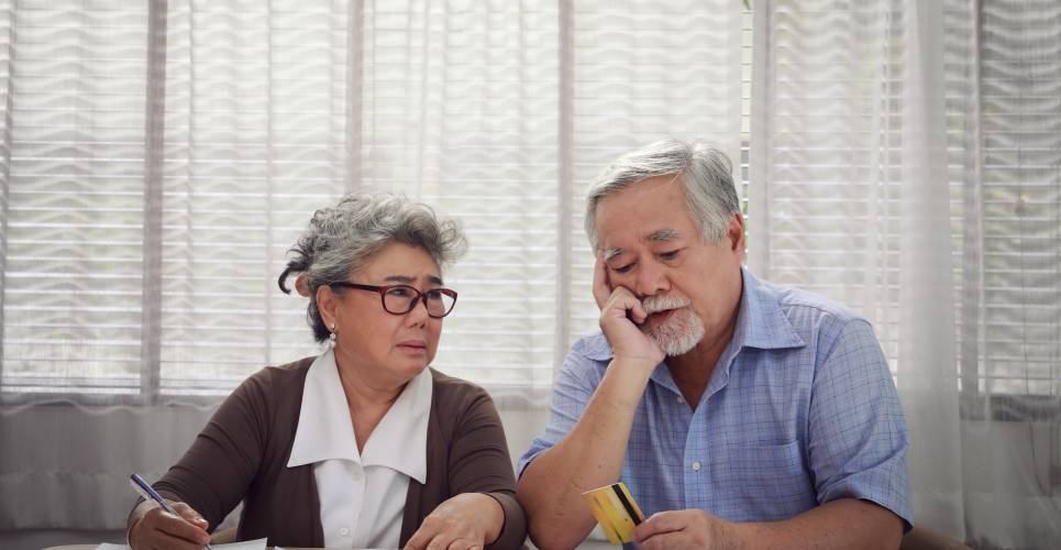 A senior couple looking stressed while sitting at a table reading documents and calculating their taxes.