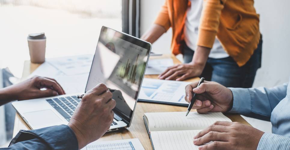 A business team meeting to discuss marketing strategies, with a laptop and paper graph documents on the table.