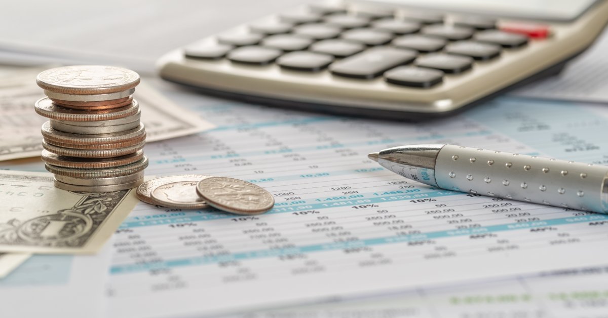 A few dollar bills underneath a stack of quarters, nickels, pennies, and dimes. The money is next to a pen and calculator.