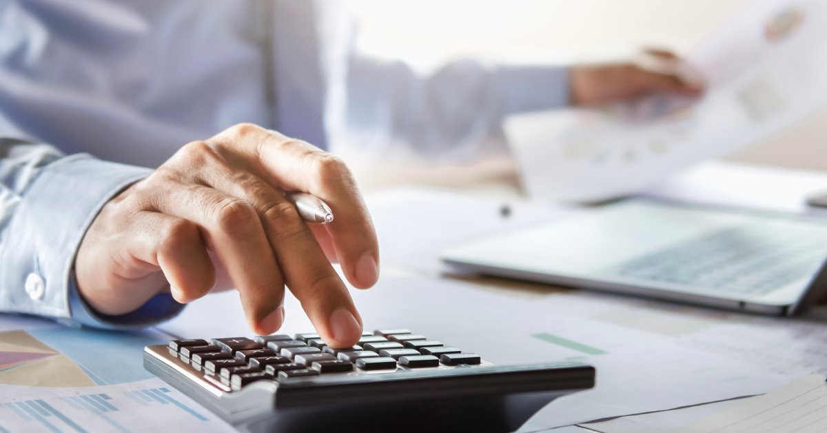 A financial expert working at their desk. They are using a calculator while looking over a finance report on a sheet of paper.