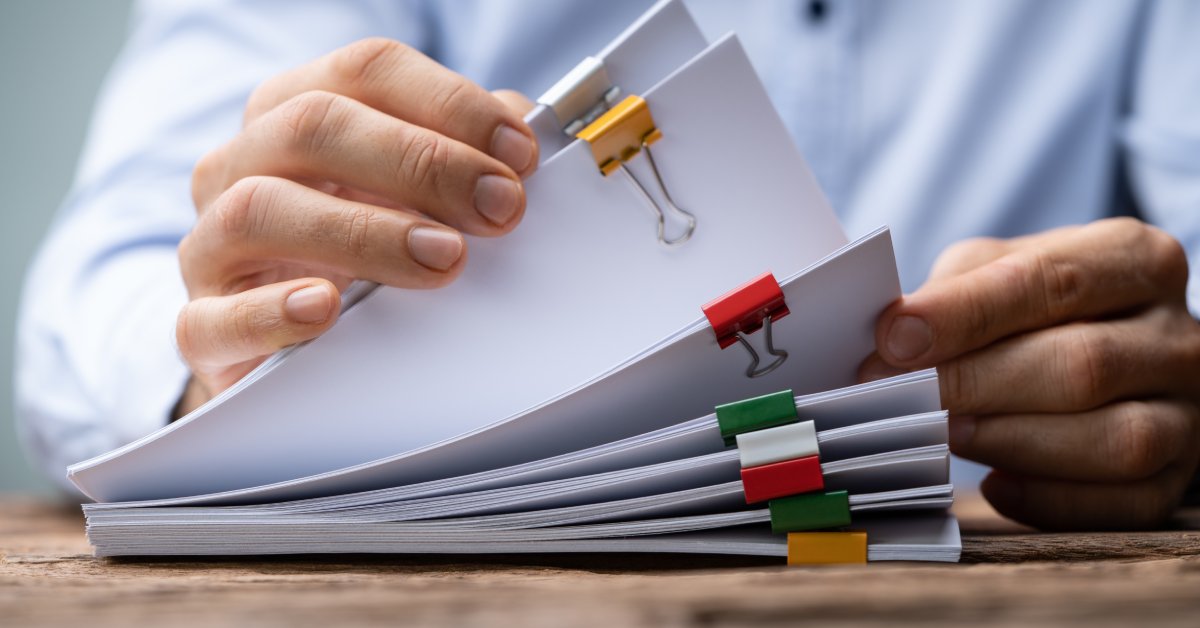 A man flipping through stacks of papers bound together with clasps colored white, yellow, red, and green.